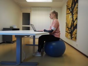 Personen sitter på en gymboll med en ergonomisk stillasittande hållning.